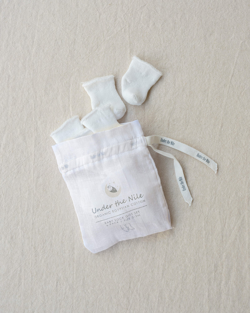 White baby booties and socks in a drawstring bag on a beige background