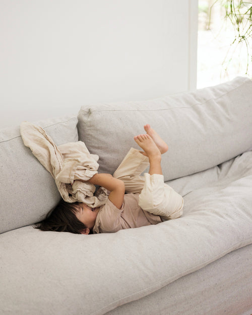Child playing on a light gray sofa with a white blanket