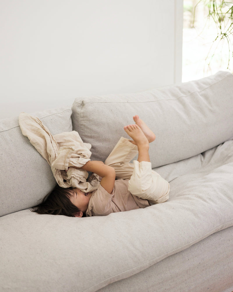 Child playing on a light gray sofa with a white blanket