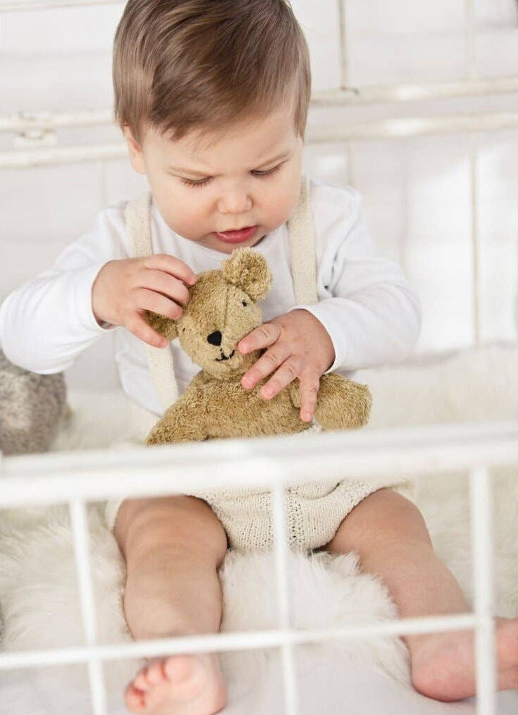 Baby playing with a teddy bear in a crib