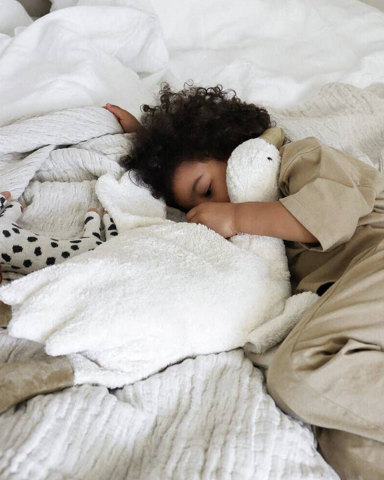 Person lying on a bed with white bedding and a plush toy