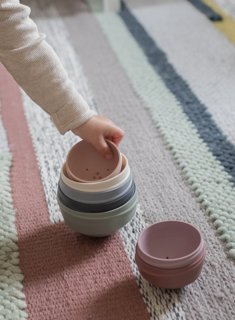 Child's hand stacking colorful silicone cups on a striped rug