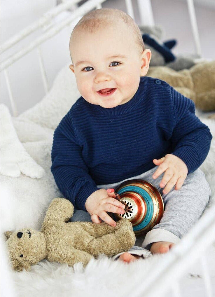 Baby sitting on a white blanket with toys, wearing a navy blue sweater.