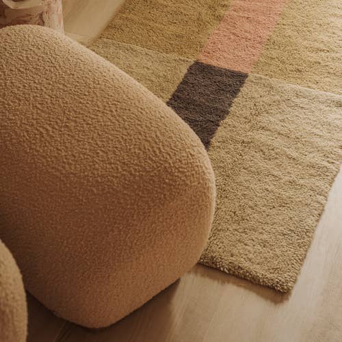 Round brown ottoman next to a geometric-patterned rug on a wooden floor.